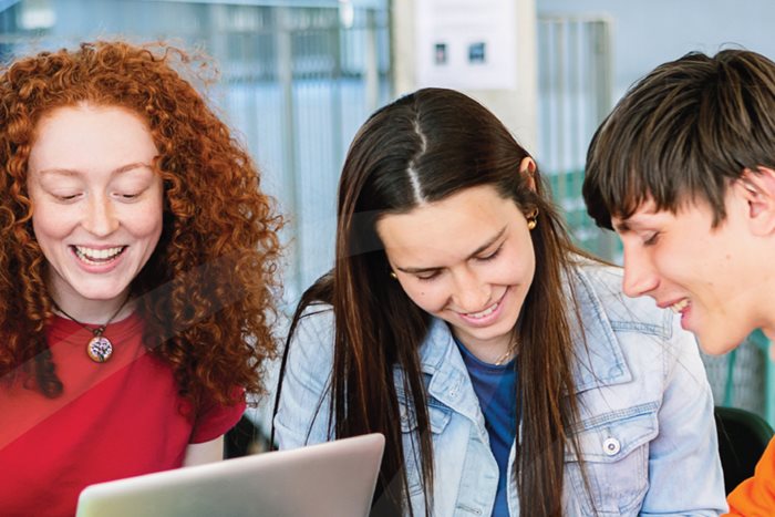 Group of students smiling while working together on a laptop in an indoor space.